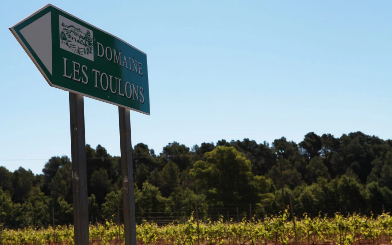 Panneau indiquant le domaine Les Toulons, au milieu de vignes et d'arbres.