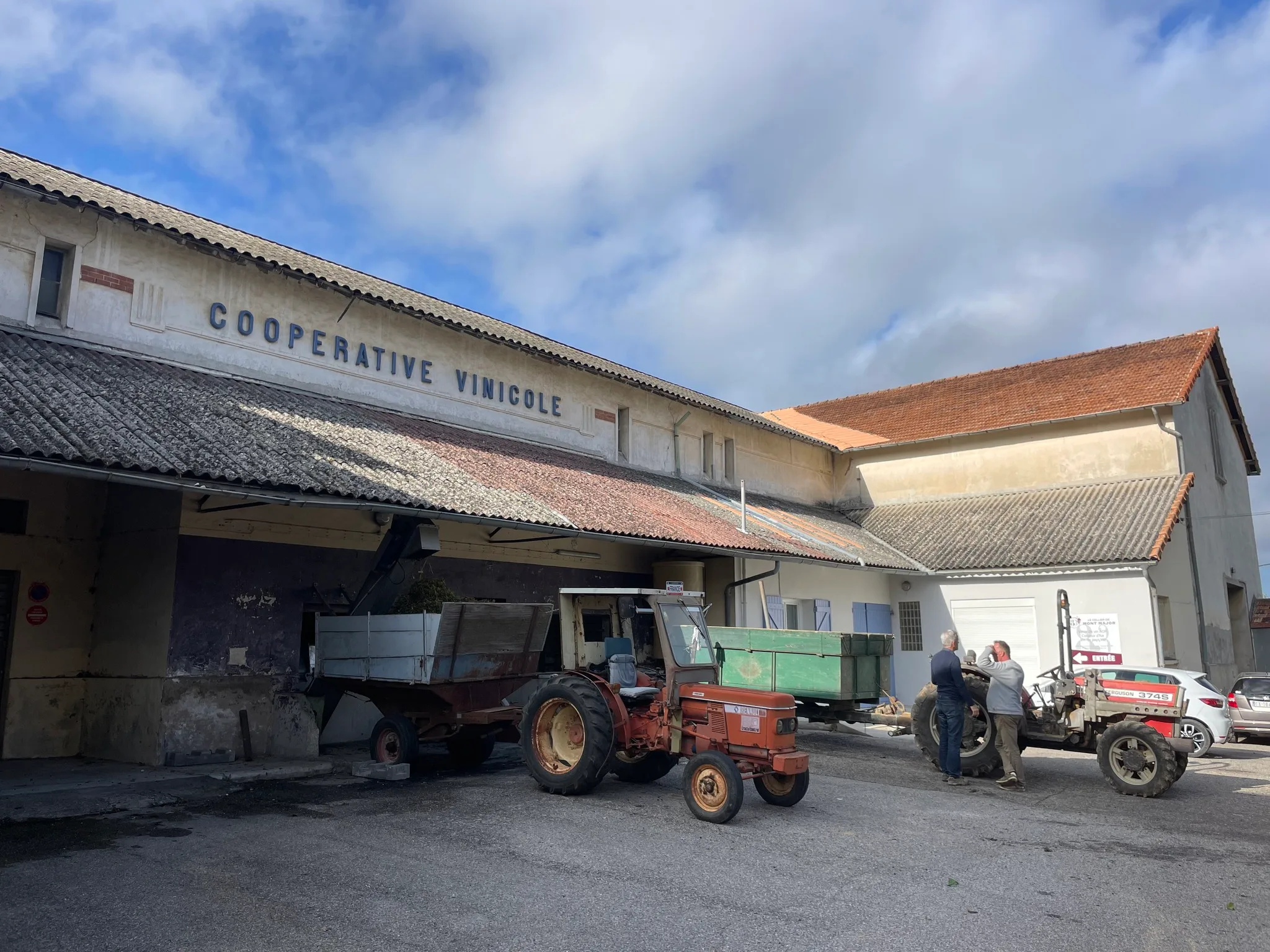 Coopérative vinicole avec des tracteurs devant, dans un paysage rural.