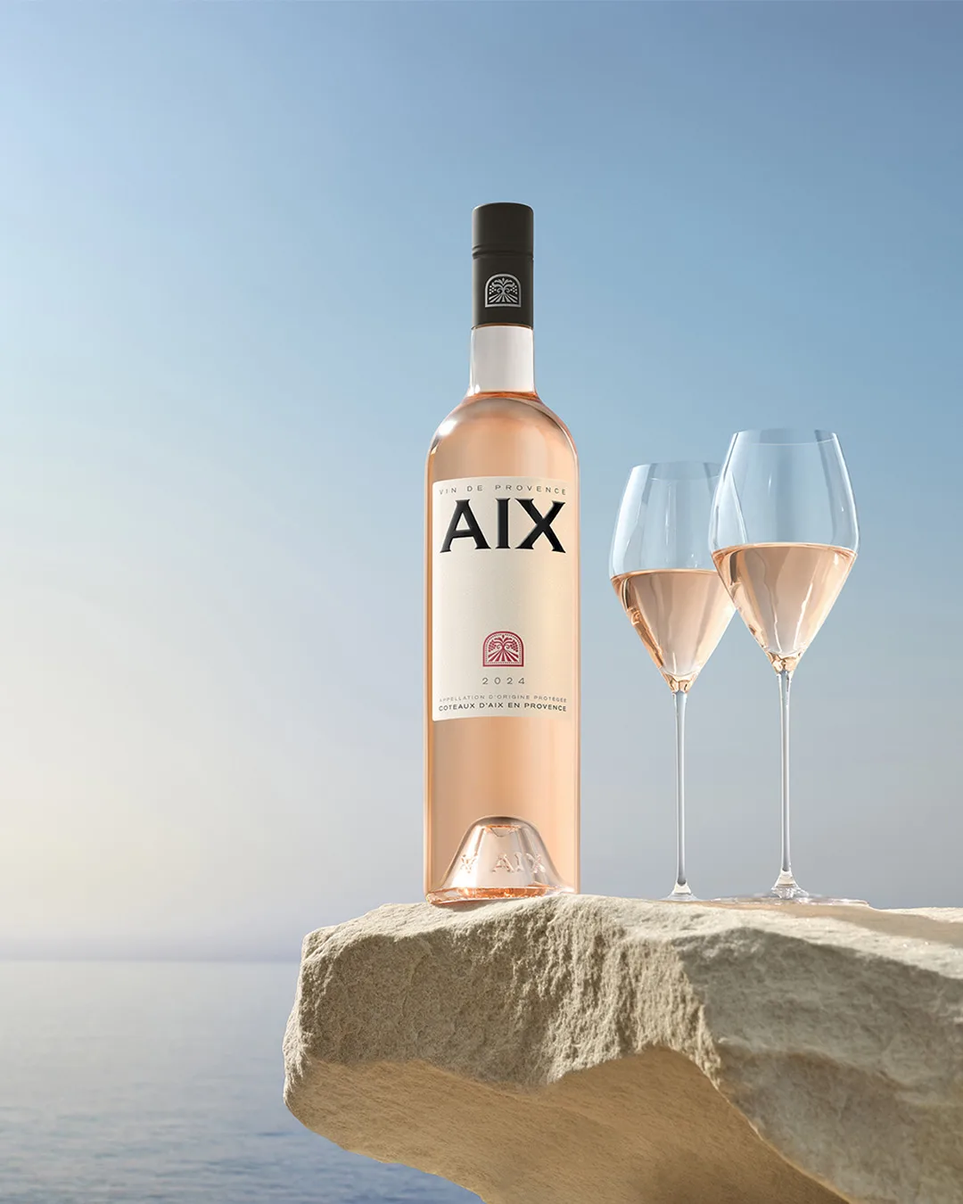 Un élégant flacon et deux verres de vin rosé Aix 2024, sur une roche méditerranéenne.