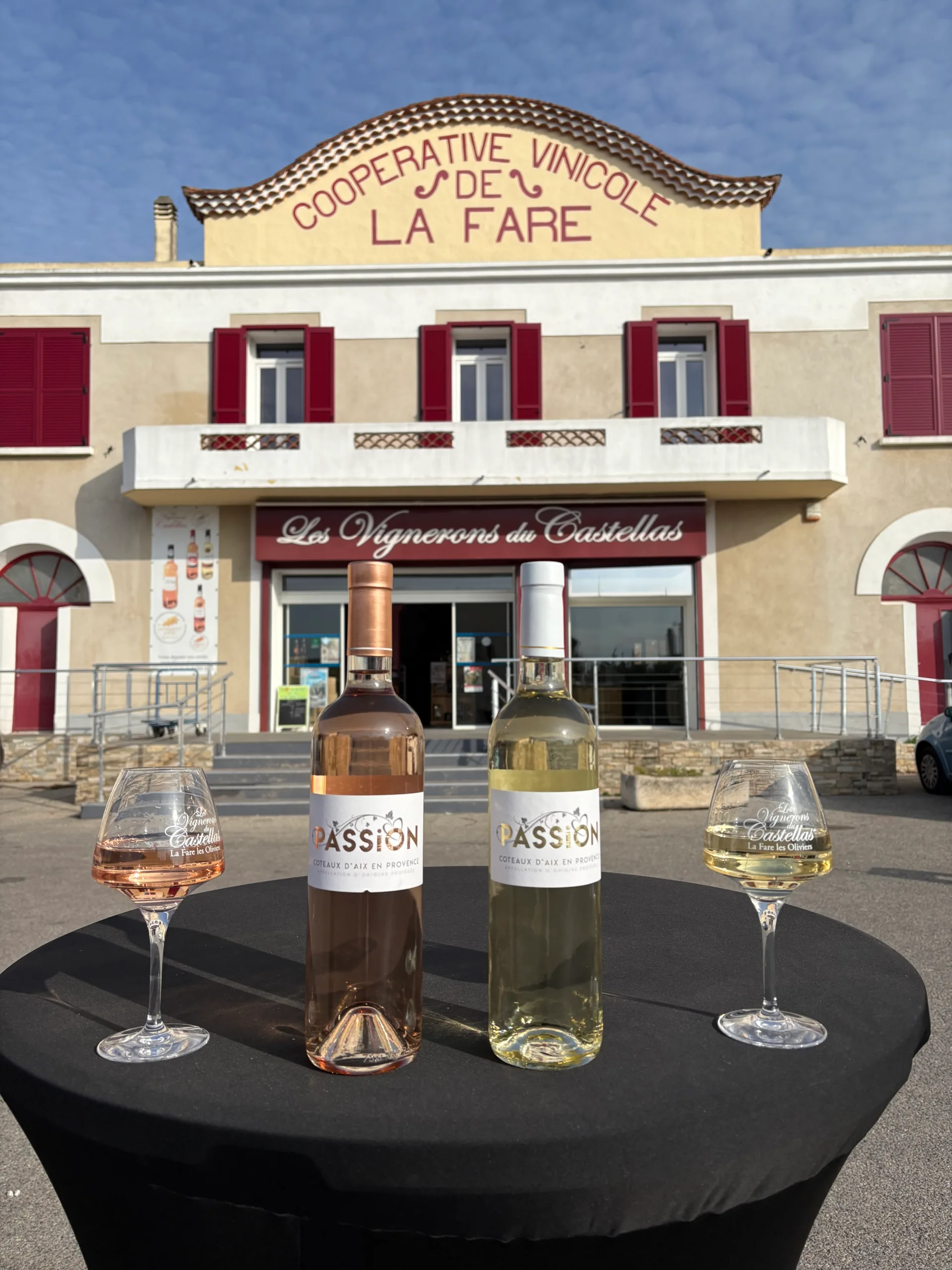 Vin rouge et blanc sur une table noire devant la façade de la coopérative La Fare.
