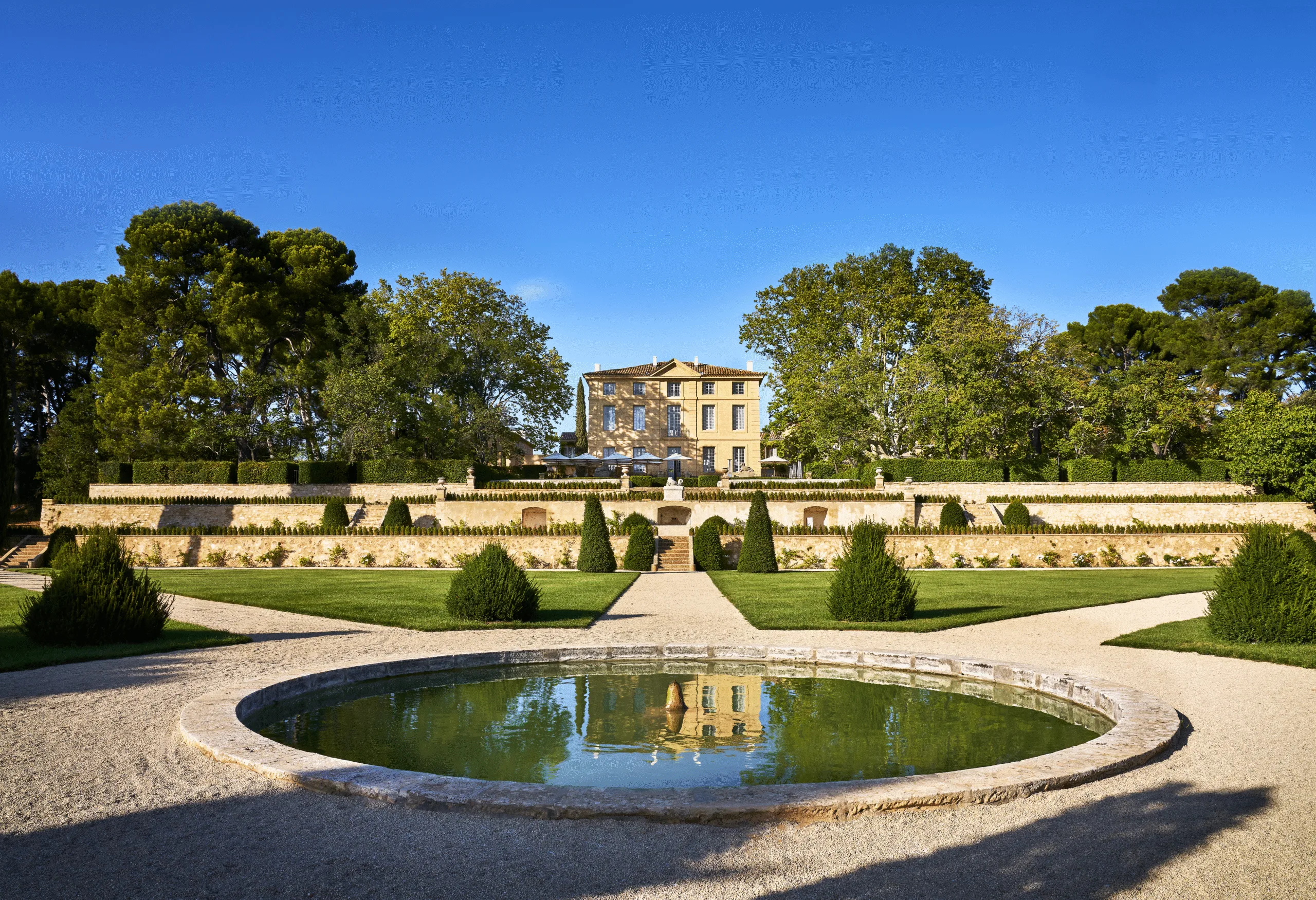 Jardin paysagé avec fontaine et château sous un ciel bleu éclatant.