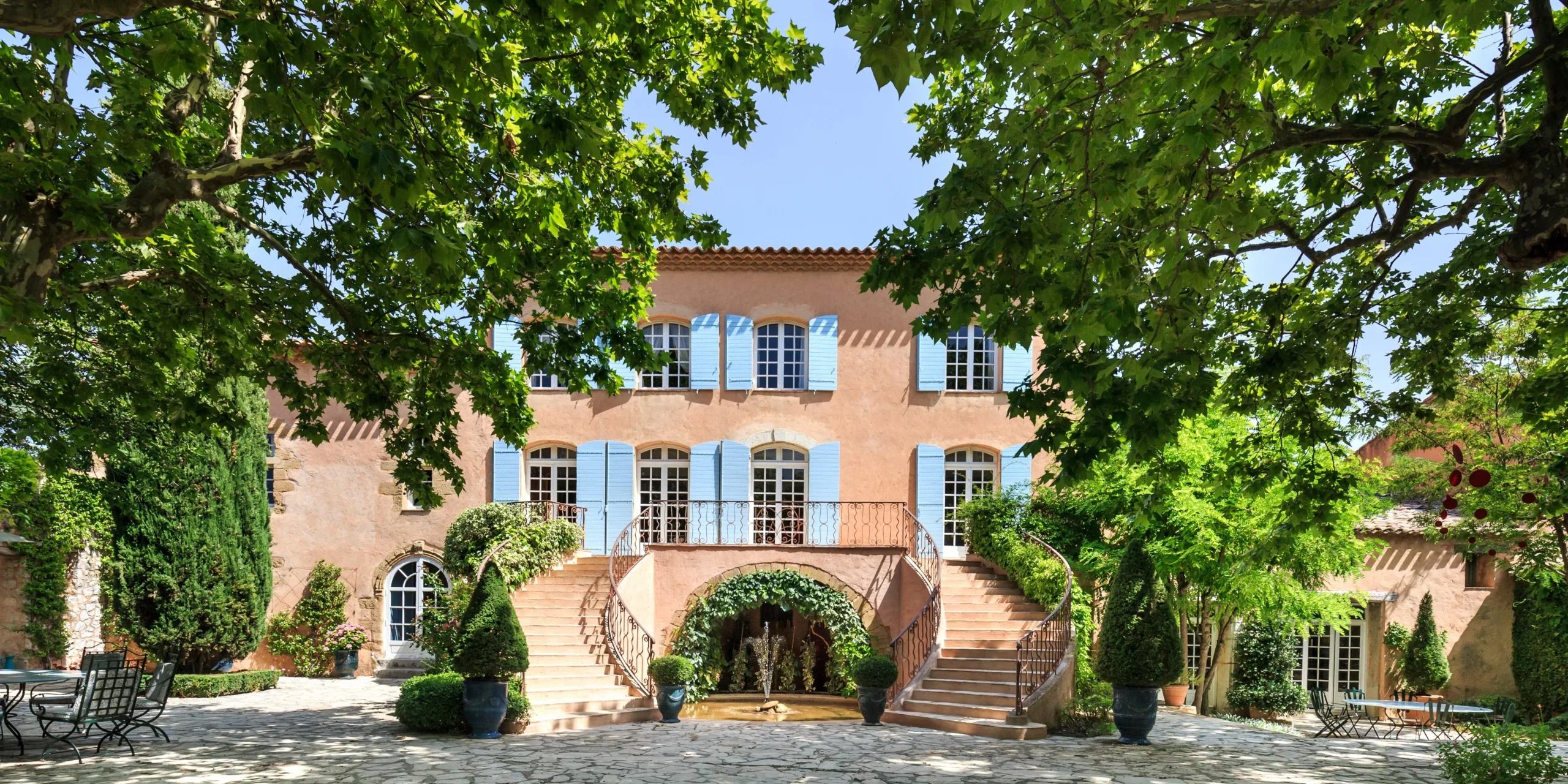 Belle demeure provençale avec des volets bleus et un jardin luxuriant.